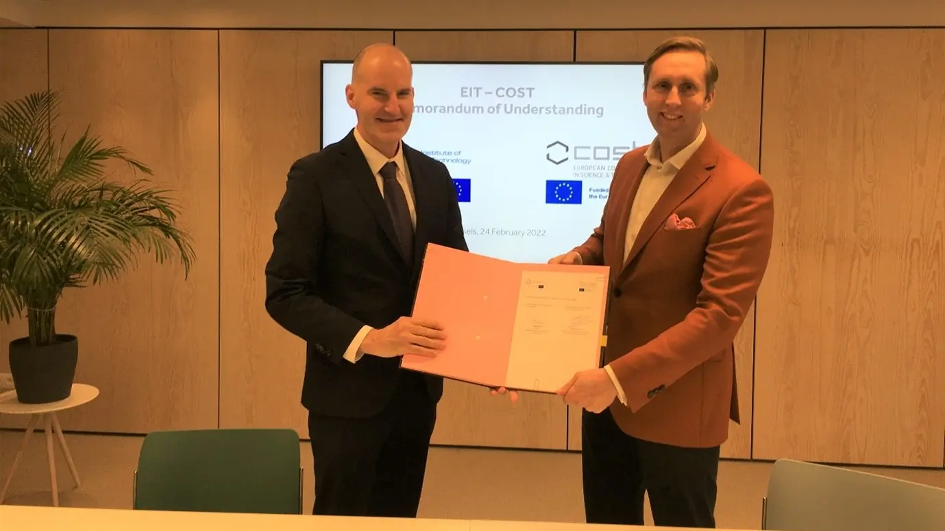 Photo of two men standing side by side jointly holding a document