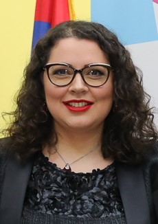 Portrait photo of a woman with long curly brown hear wearing glasses dressed in a black suit