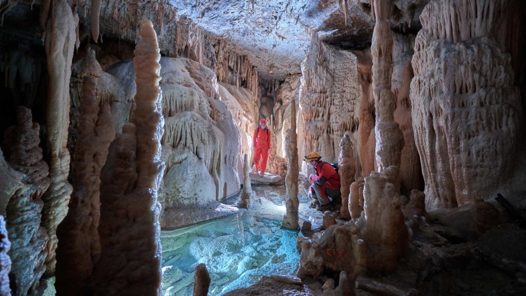 Underground-photo of two speleologists in a cave with stalactites and underground river