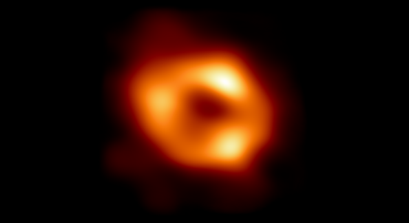 Photo of a black hole - a red/orange donut shaped ring with spots of white light with a black center