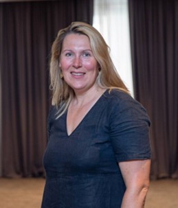 Profile photo of a woman with long blond hair wearing a navy blue top smiling to camera
